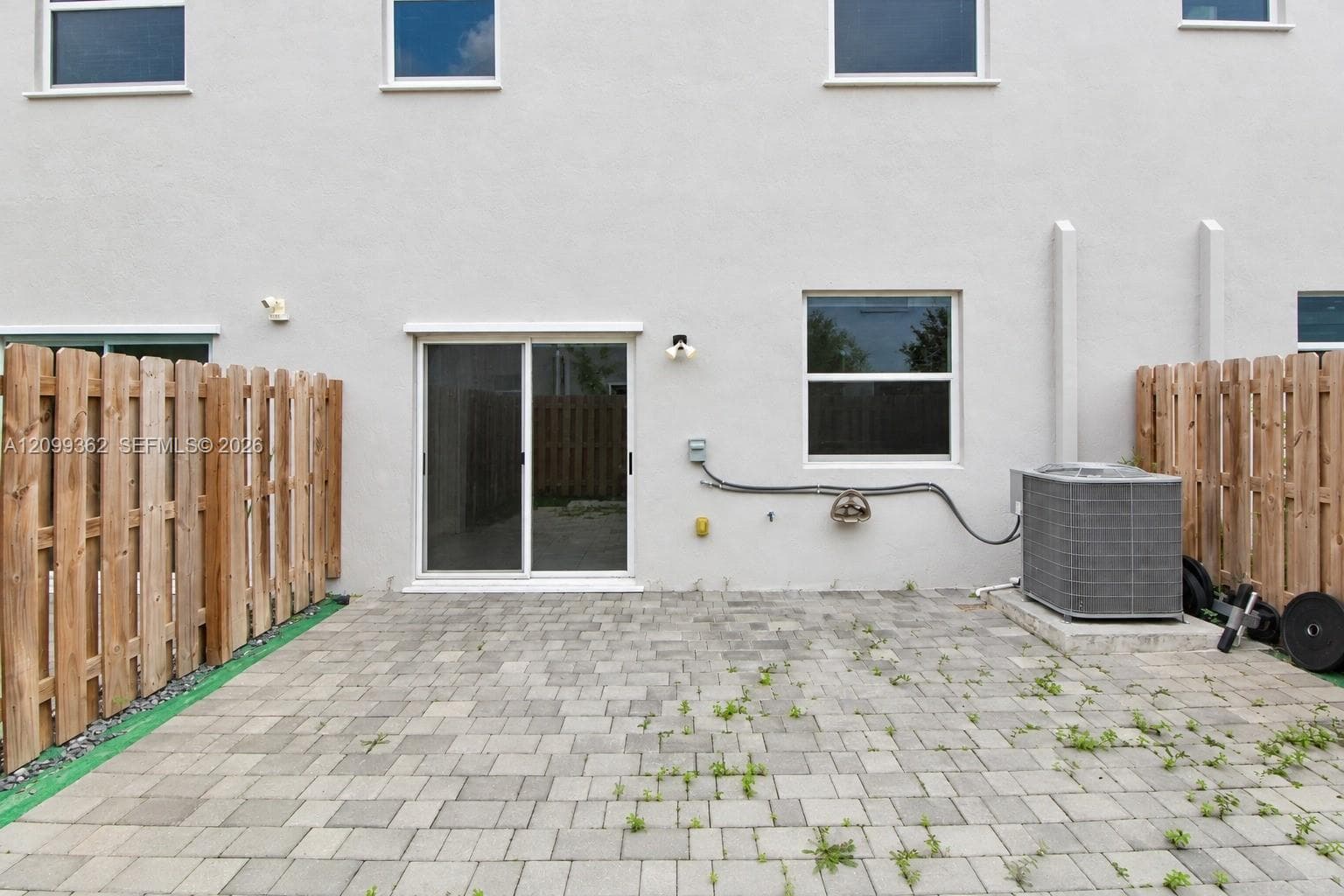 Exterior patio featuring stone-paver hardscaping, enclosed by vertical wood privacy fencing, including sliding glass door access and exterior wall-mounted lighting