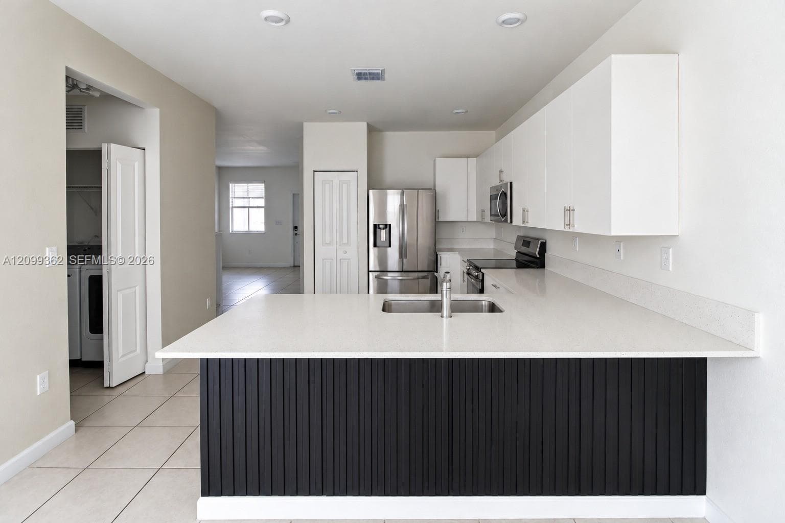 Kitchen featuring an expansive stone countertop, stainless steel appliances, flat-panel white cabinetry, a dual-basin undermount sink, and a vertical-slat kitchen island facade