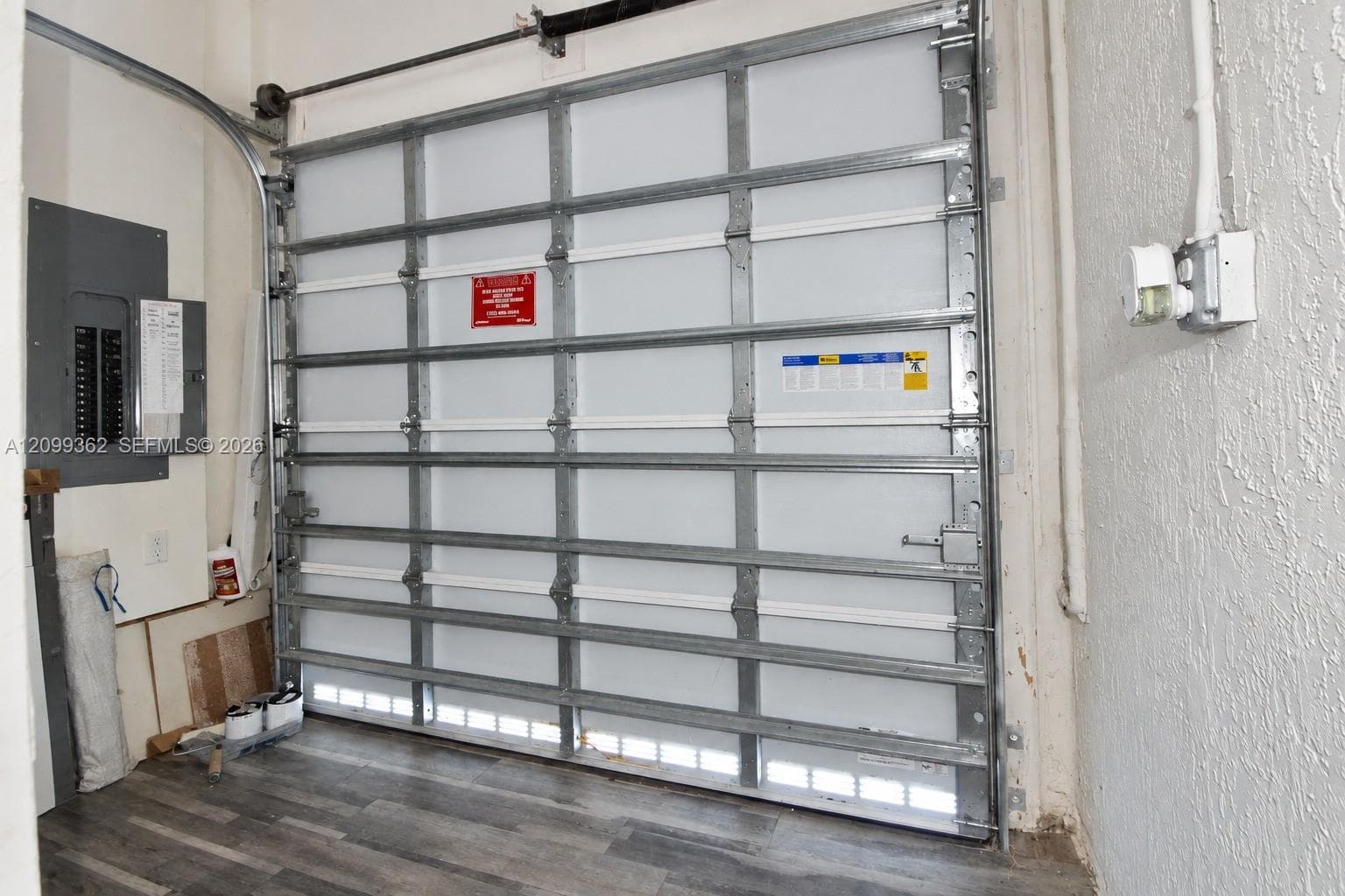 Sectional garage door with metal tracking, installed electrical panel, and wood-finish flooring