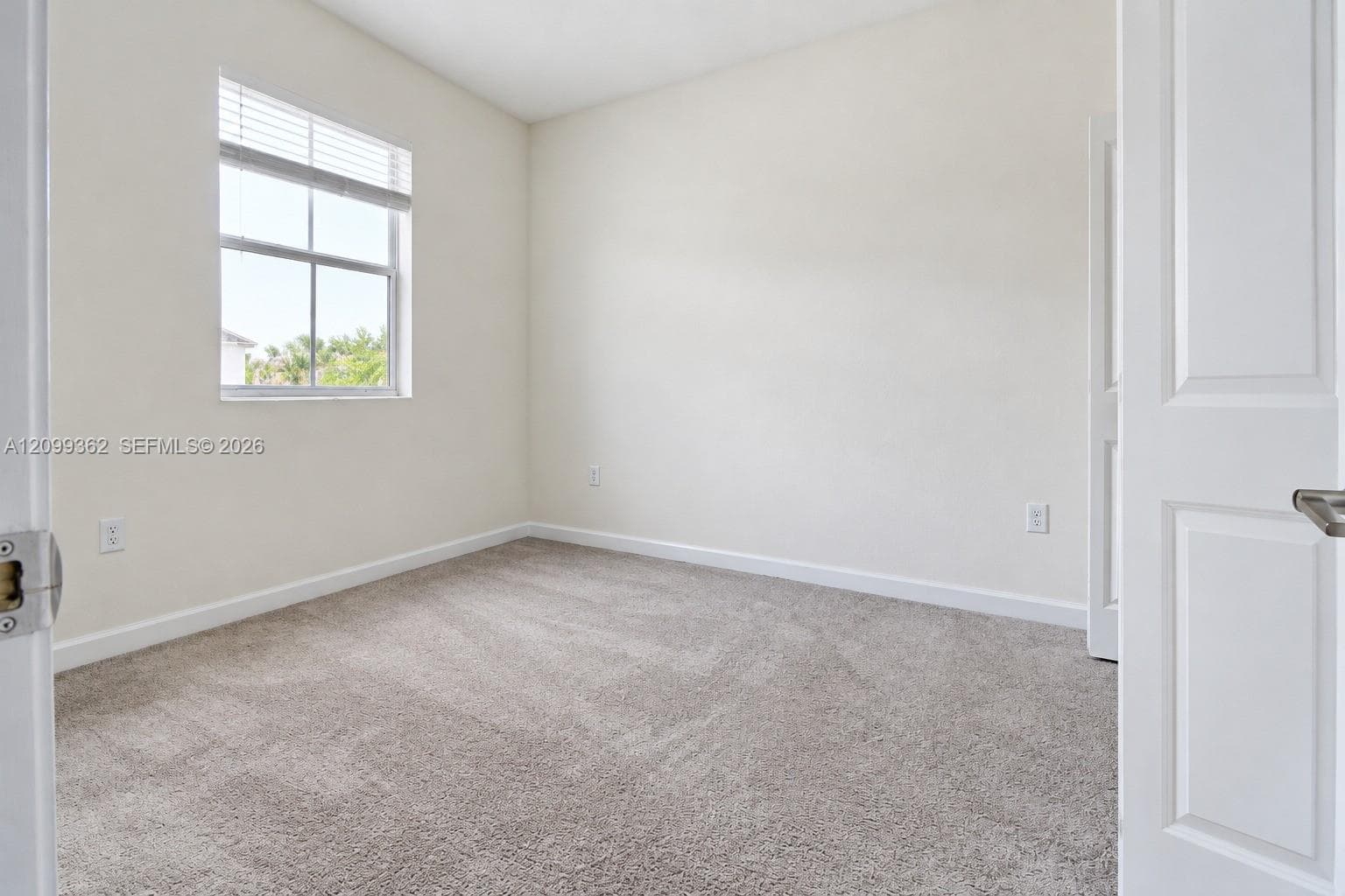 Neutral-toned carpet flooring, neutral wall paint, and a multi-pane window with adjustable blinds