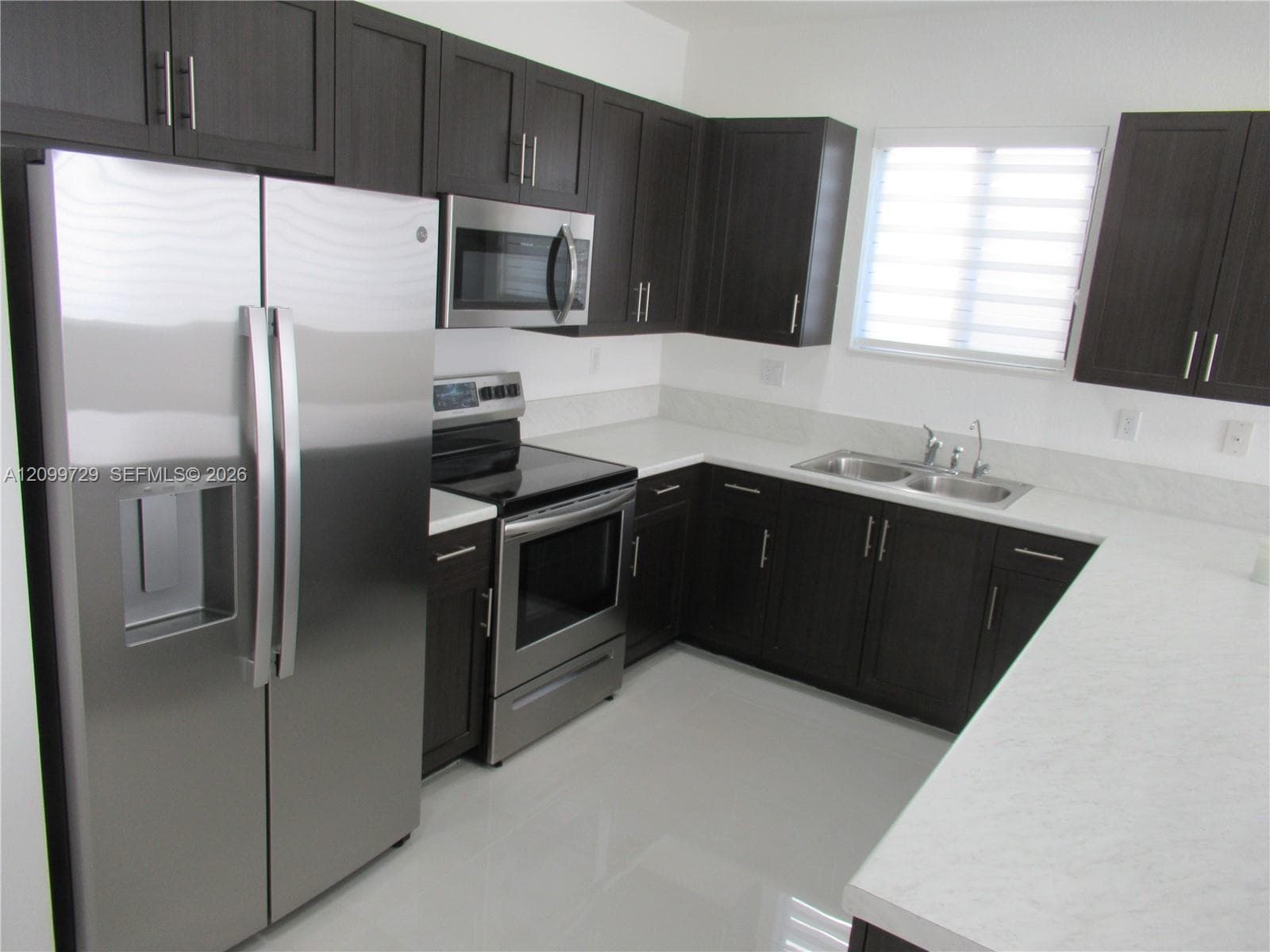 Kitchen featuring dark wood-finish cabinetry, solid-surface countertops, a dual-basin stainless steel sink, and stainless steel appliances