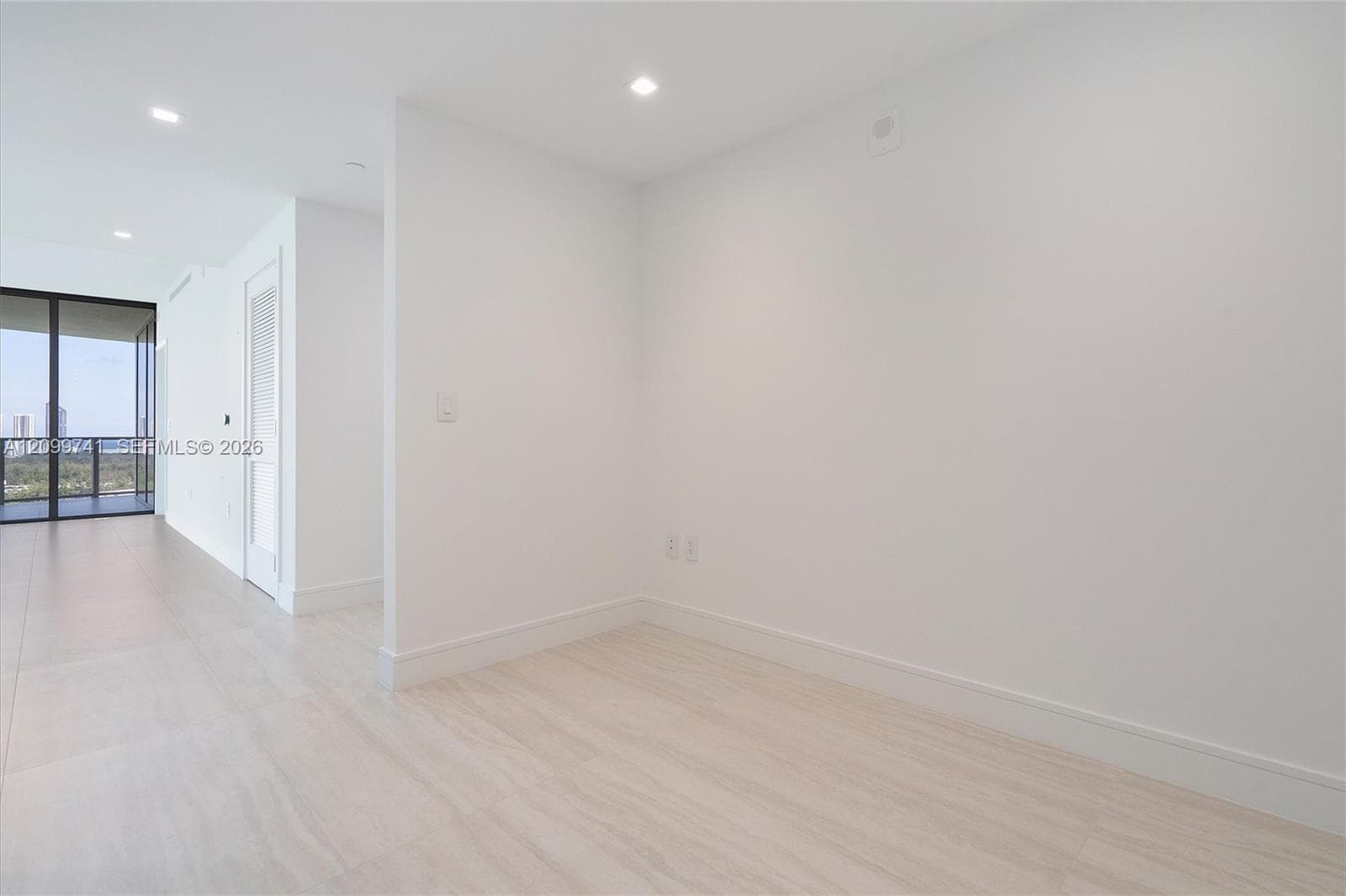 Neutral-toned tile flooring, recessed ceiling lighting, and floor-to-ceiling glass door leading to a balcony