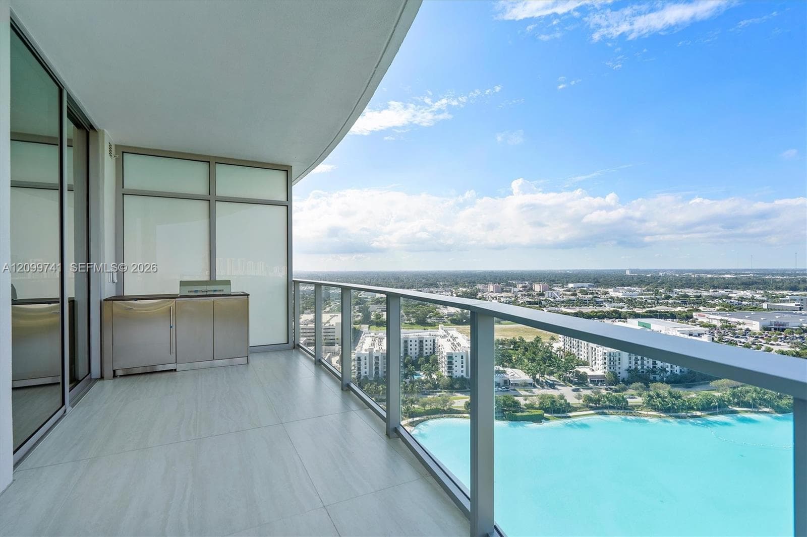 Covered terrace featuring large-format tile flooring, a built-in stainless steel outdoor kitchen station, and a frameless glass balcony railing