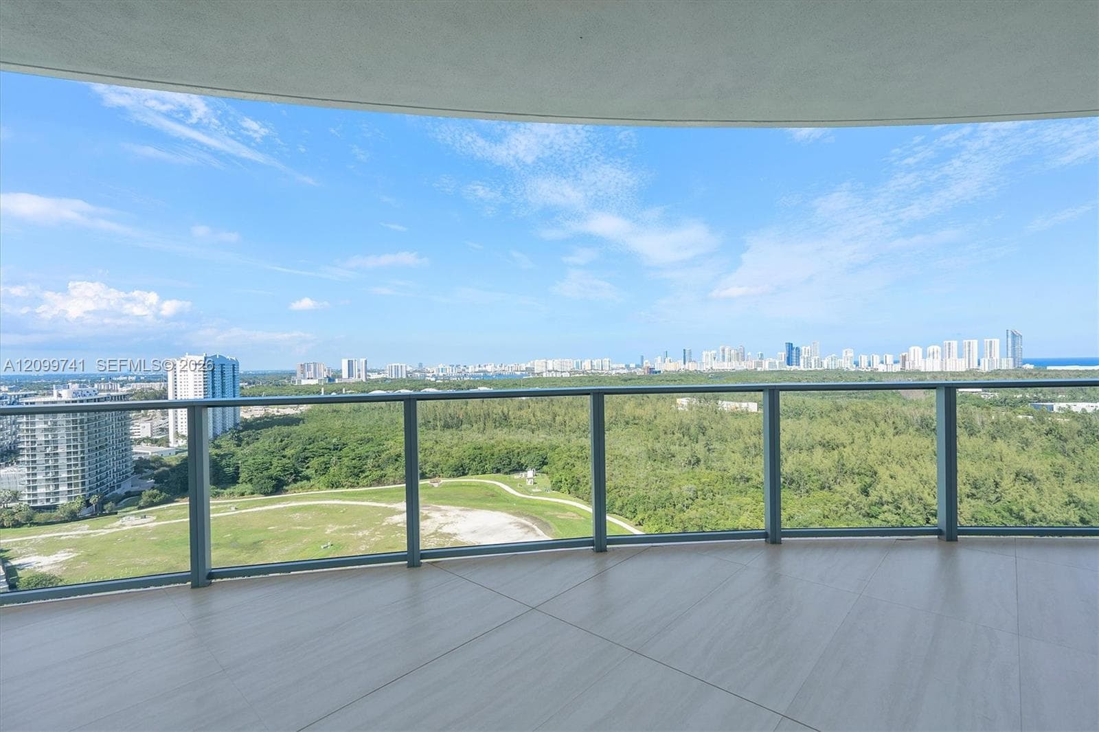 Expansive covered balcony featuring large-format tile flooring and a minimalist glass-panel railing
