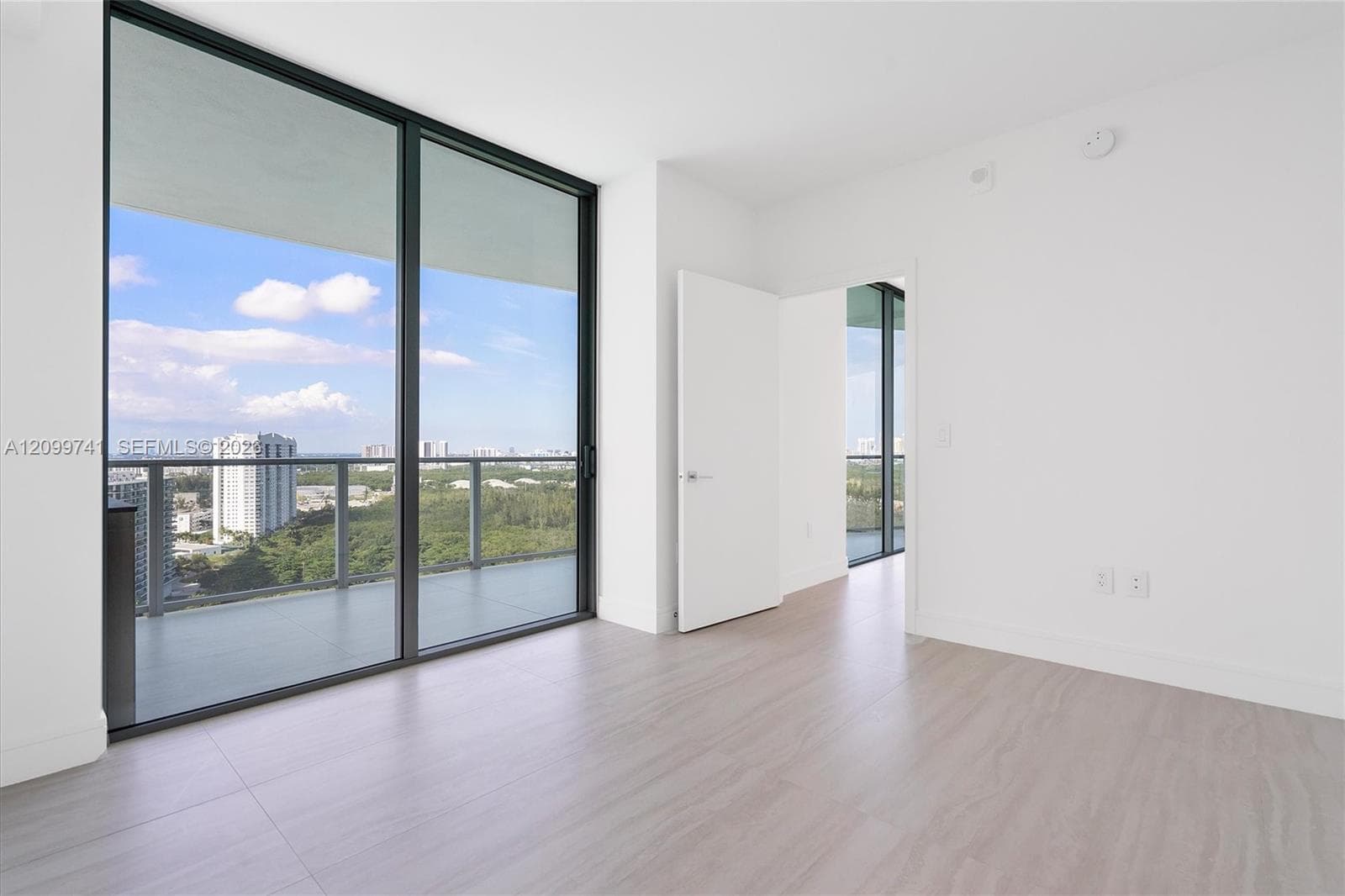 Floor-to-ceiling glass sliding doors, private balcony with metal railing, wood-finish flooring, and crisp white walls