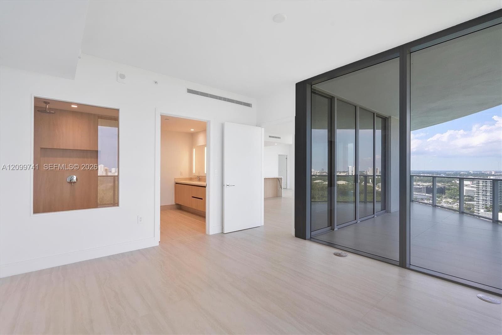 Floor-to-ceiling glass sliding doors, private covered balcony, integrated wood-finish cabinetry, recessed ceiling lighting, and wood-finish flooring