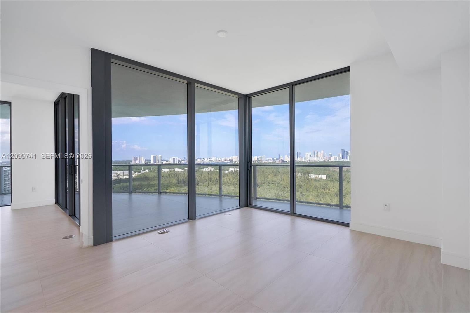 Floor-to-ceiling glass corner windows, wraparound covered balcony with glass railing, wood-finish flooring, and neutral wall finishes