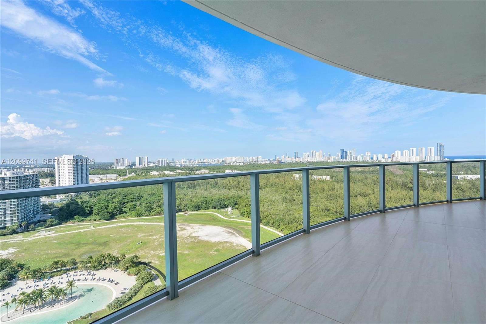 Spacious covered balcony with tile flooring and a glass panel railing, featuring panoramic scenery of the surrounding landscape and coastal cityscape
