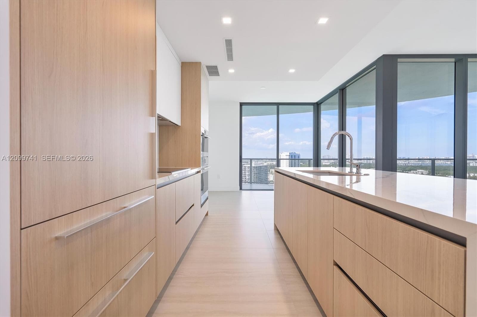 Kitchen featuring wood-finish cabinetry, an expansive central island with a solid-surface countertop, floor-to-ceiling glass windows, recessed lighting, and built-in stainless steel appliances