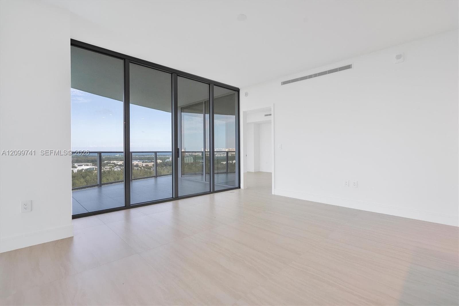 Floor-to-ceiling glass sliding doors, wood-finish flooring, recessed ceiling lighting, and covered balcony with metal railing