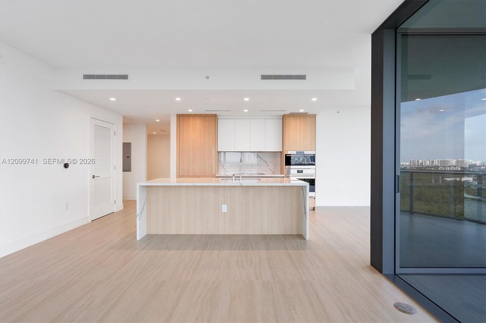 Kitchen featuring a central island with a stone-finish countertop, dual-tone wood-finish and matte-white cabinetry, built-in stainless steel wall ovens, and wood-finish flooring throughout