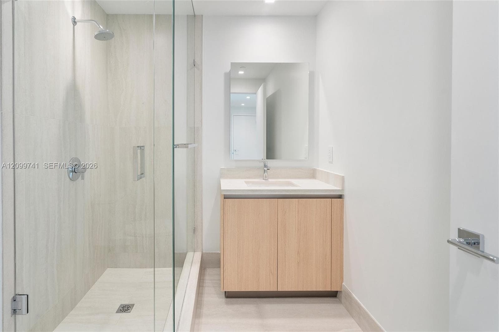 Walk-in shower with a glass enclosure, light wood-finish vanity, rectangular undermount sink, solid surface countertop, and wall-mounted vanity mirror