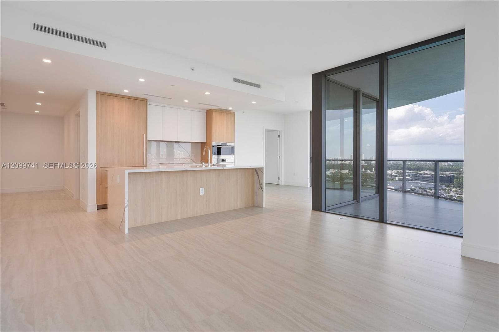 Kitchen featuring a waterfall-edge island, light wood-finish cabinetry, floor-to-ceiling glass wall, and balcony
