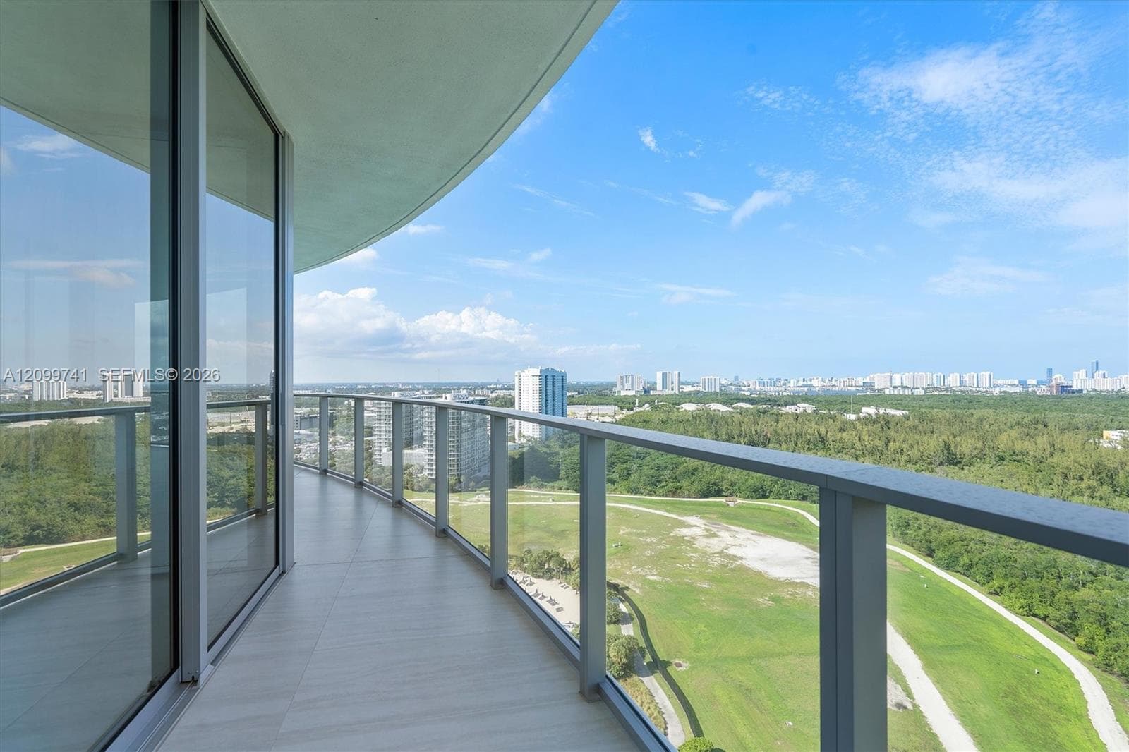 Curved private balcony featuring large-format tile flooring, a metal railing with glass panels, and floor-to-ceiling glass wall panels