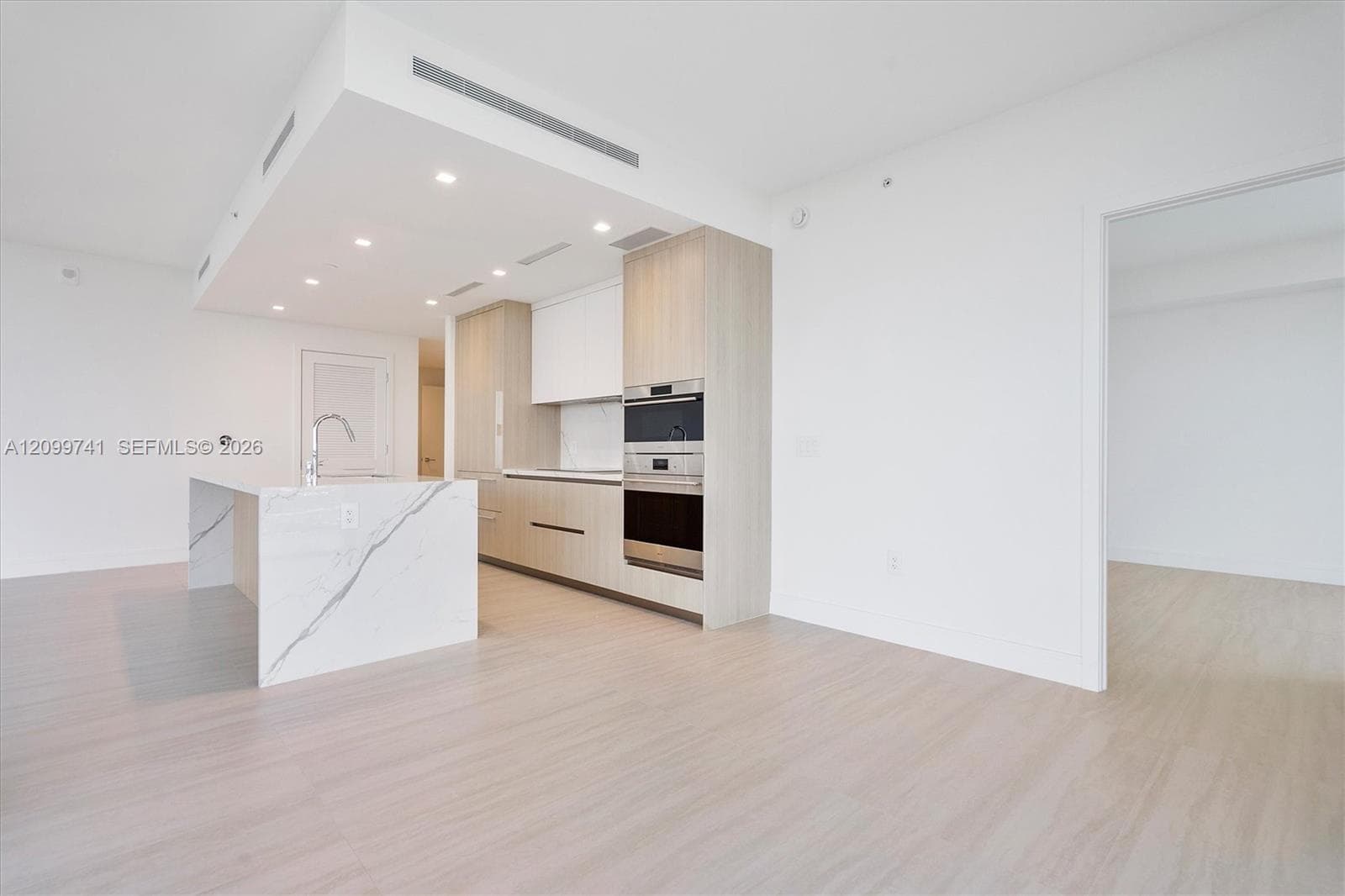 Kitchen featuring wood-finish cabinetry, stone-surfaced waterfall island, recessed lighting, and built-in stainless steel appliances