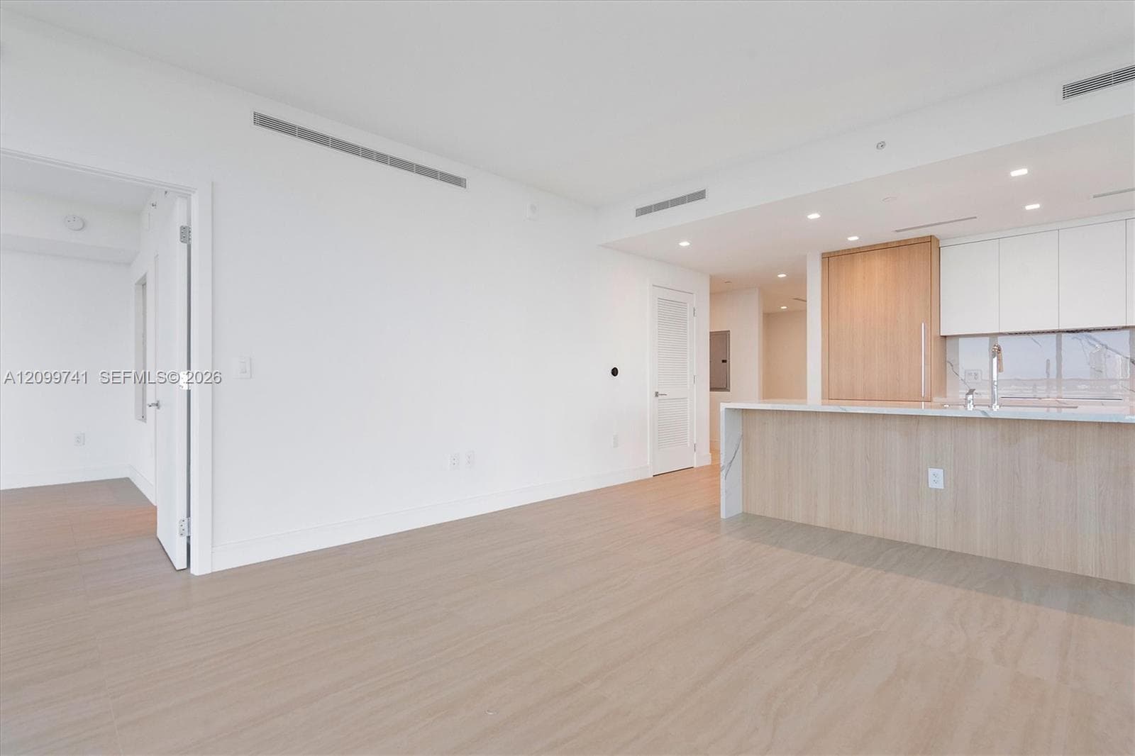 Open-concept interior featuring light wood-finish flooring, recessed lighting, sleek white cabinetry, a wood-finish kitchen island, and smooth solid-surface countertops