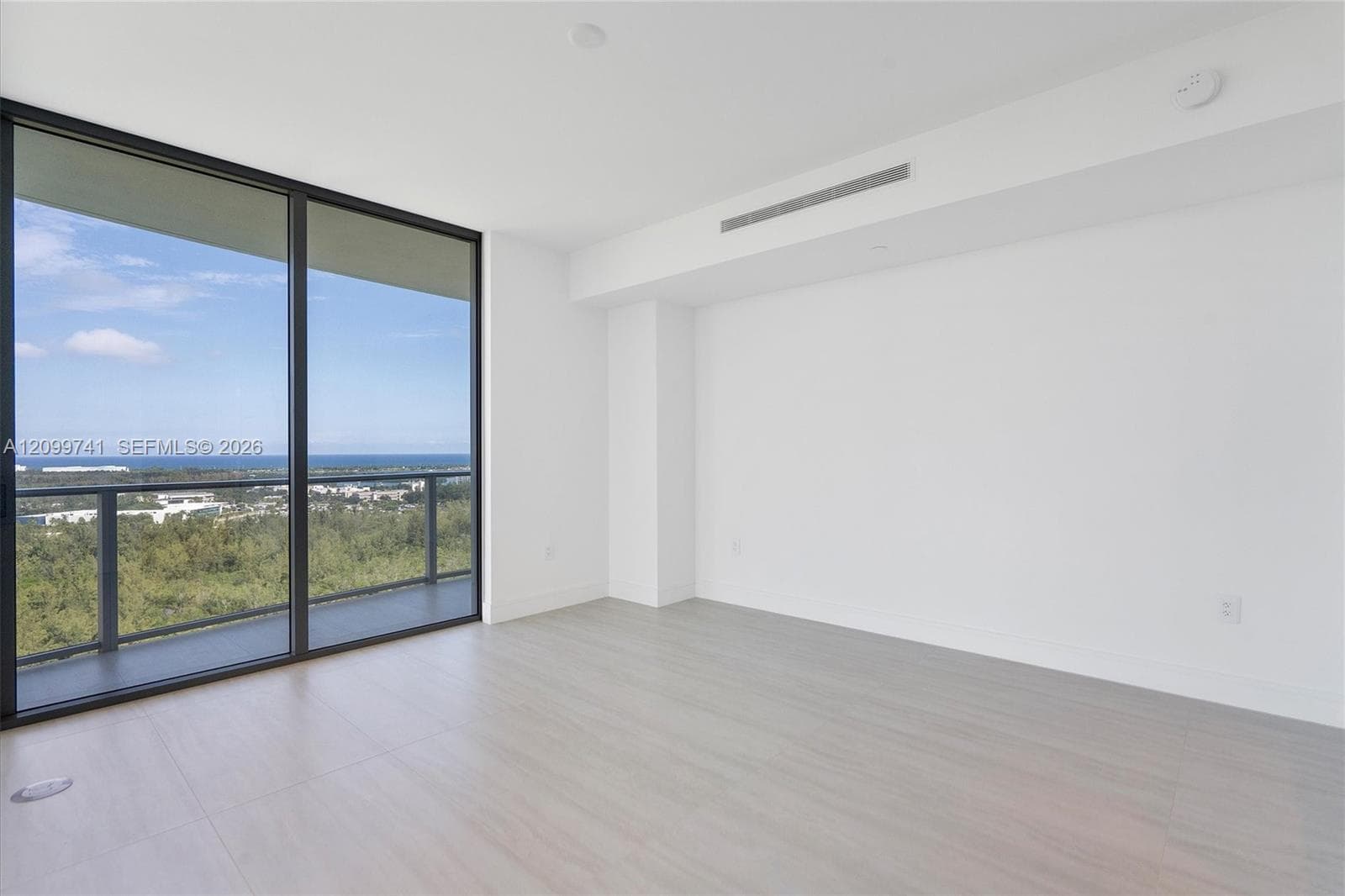 Floor-to-ceiling glass sliding doors, private balcony with metal railing, light-tone wood-finish flooring, and recessed climate control integration
