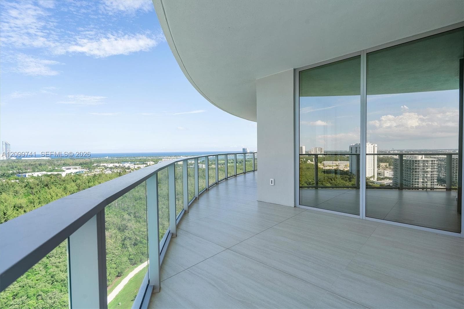 Curved private terrace featuring large-format tile flooring, a glass panel railing, and expansive floor-to-ceiling sliding glass doors