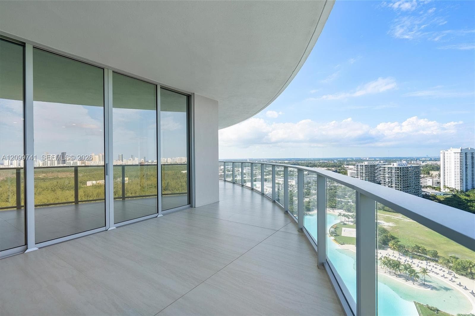 Expansive curved balcony featuring floor-to-ceiling glass sliding doors, large-format tile flooring, and a glass-paneled railing