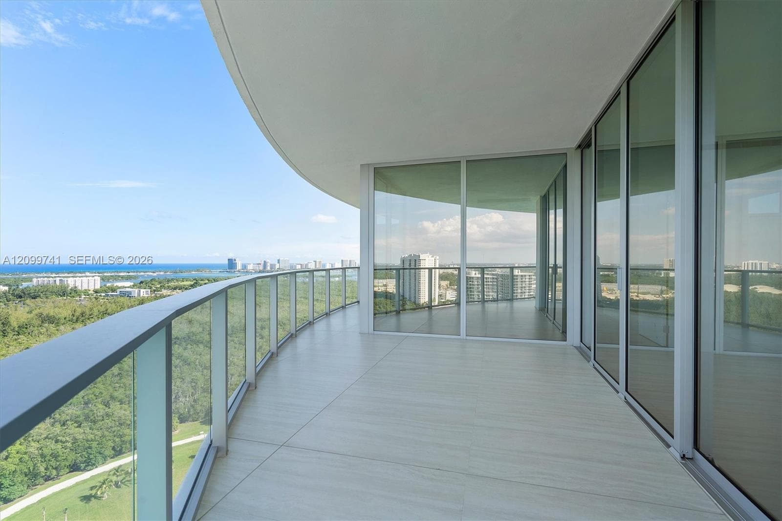 Expansive wraparound balcony featuring large-format tile flooring, a sleek glass railing system, and full-height sliding glass walls