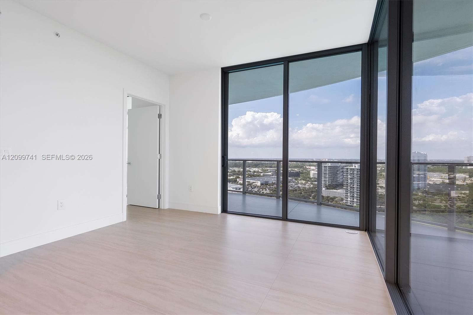 Floor-to-ceiling glass walls, wrap-around balcony access, wood-finish flooring, and minimalist white interior walls