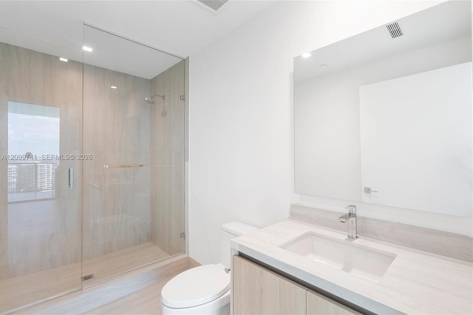 Bathroom featuring a stone-finish vanity with an integrated rectangular sink, wall-mounted mirror, walk-in shower with a glass enclosure, and light-toned, wood-finish cabinetry