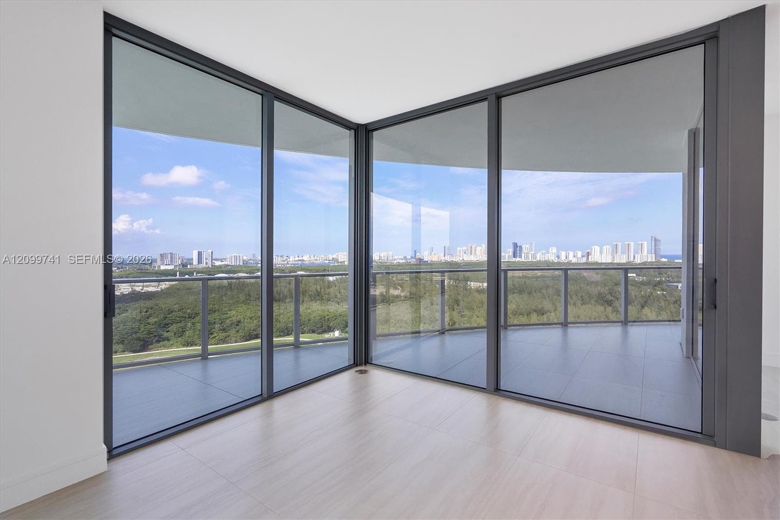 Floor-to-ceiling glass corner walls, sliding glass doors, neutral tile flooring, and a wraparound balcony with metal railings