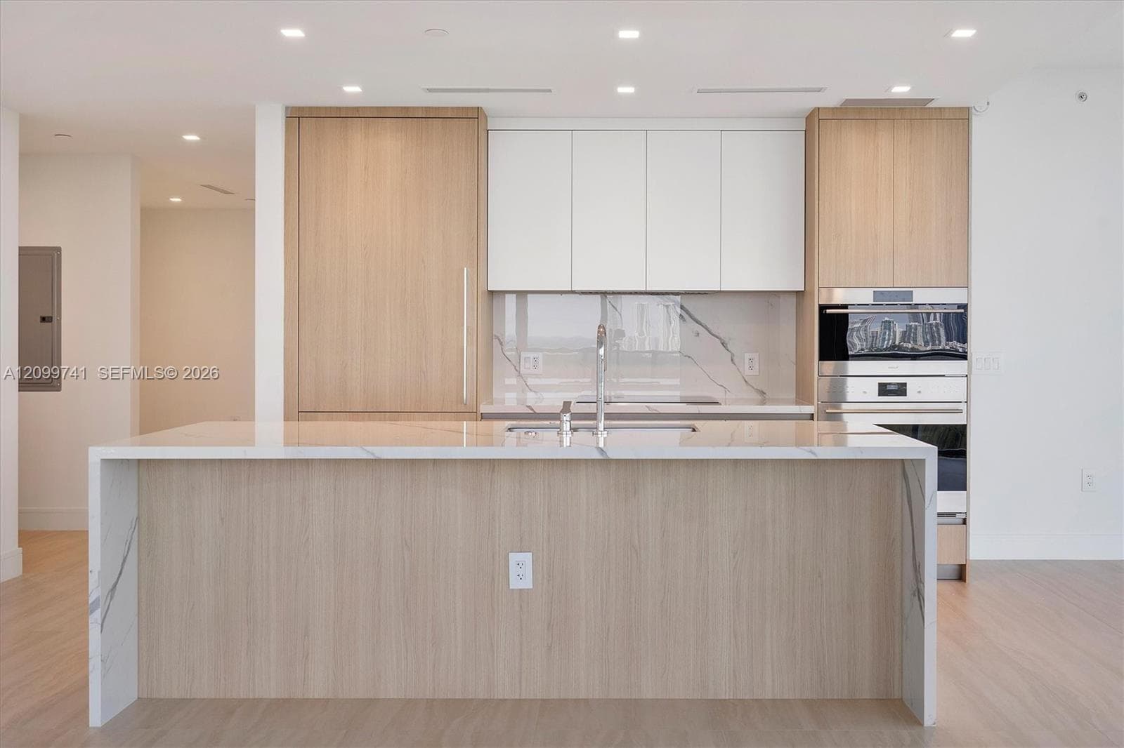 Kitchen featuring a central island with a waterfall-edge stone countertop, custom two-tone cabinetry, stone slab backsplash, and integrated stainless steel wall oven and microwave