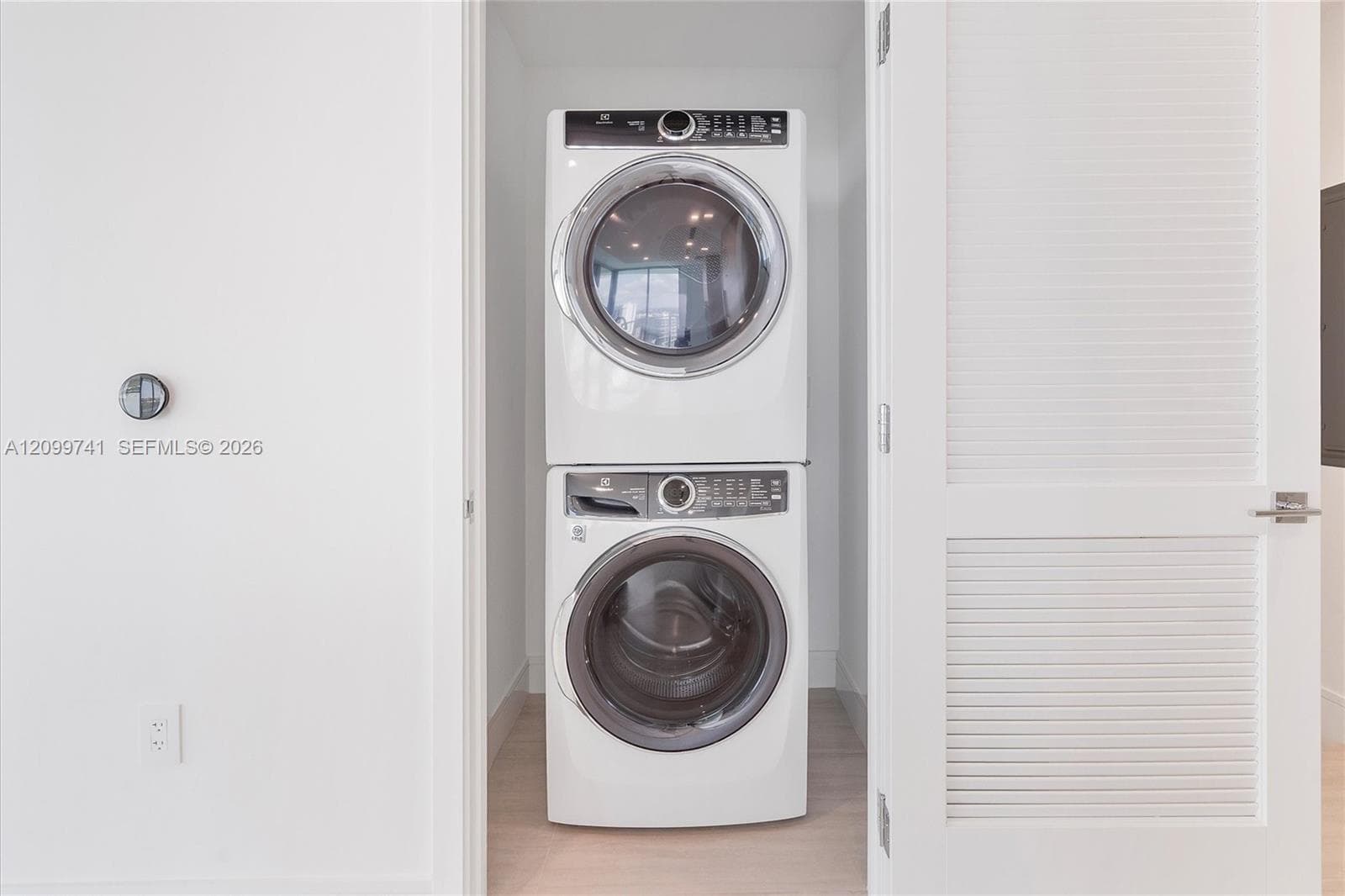 Stacked laundry center featuring white front-load appliances and louvered closet doors
