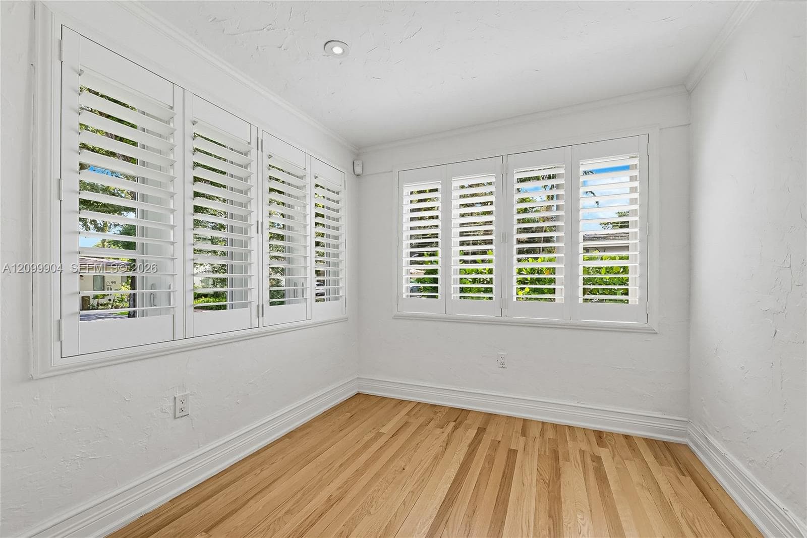 Room featuring wood-finish flooring, white walls, and multiple windows with adjustable white plantation shutters