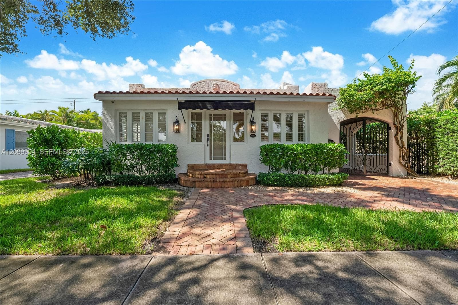 Spanish-style exterior featuring a clay tile roof, stucco facade, arched gate, brick paver walkway, and stone-tread entry steps