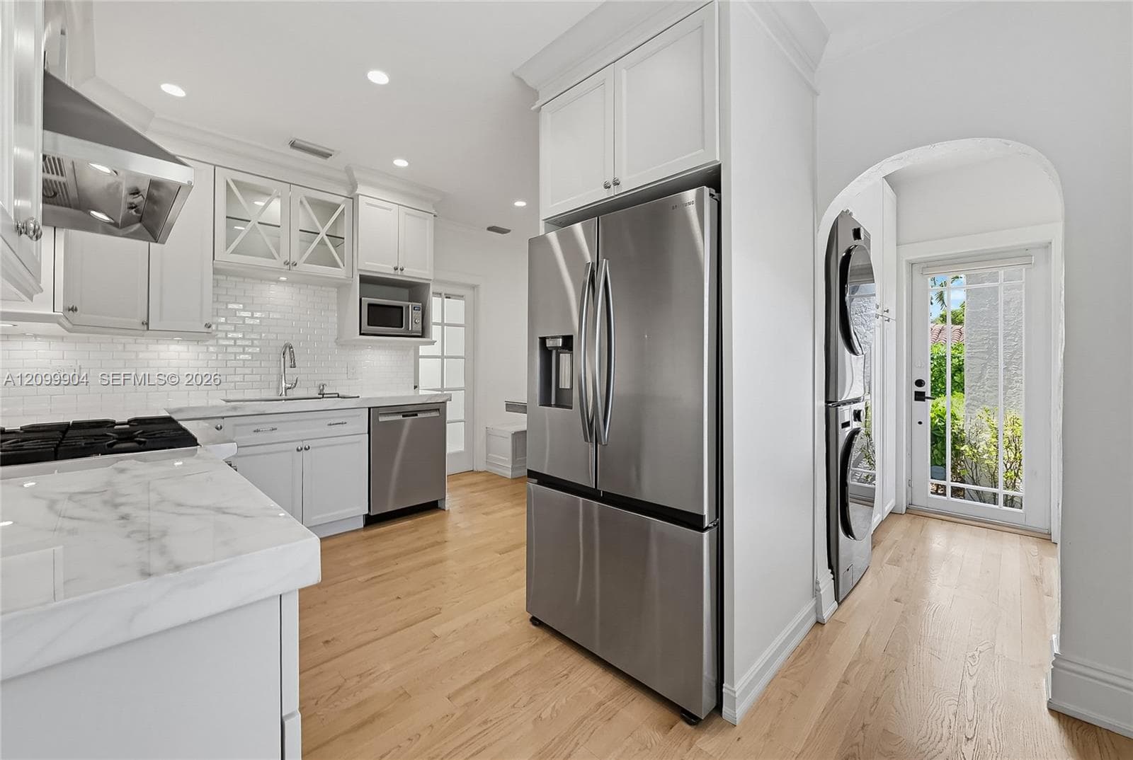 Kitchen featuring white shaker-style cabinetry, stone countertops, subway tile backsplash, stainless steel appliances, and wood-finish flooring