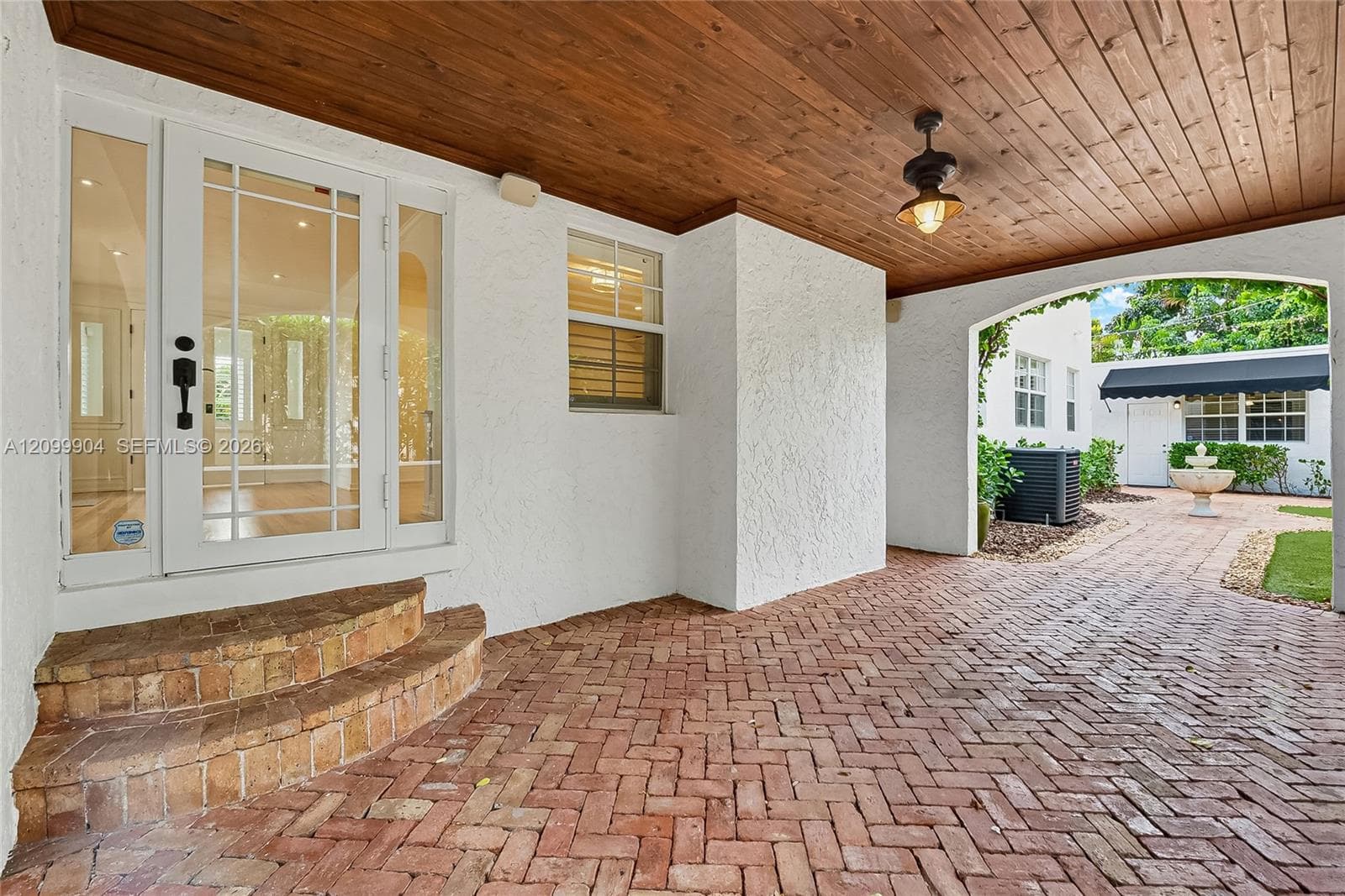 Covered entryway featuring a wood-plank ceiling, herringbone brick paving, and a glass-paneled entry door with sidelights