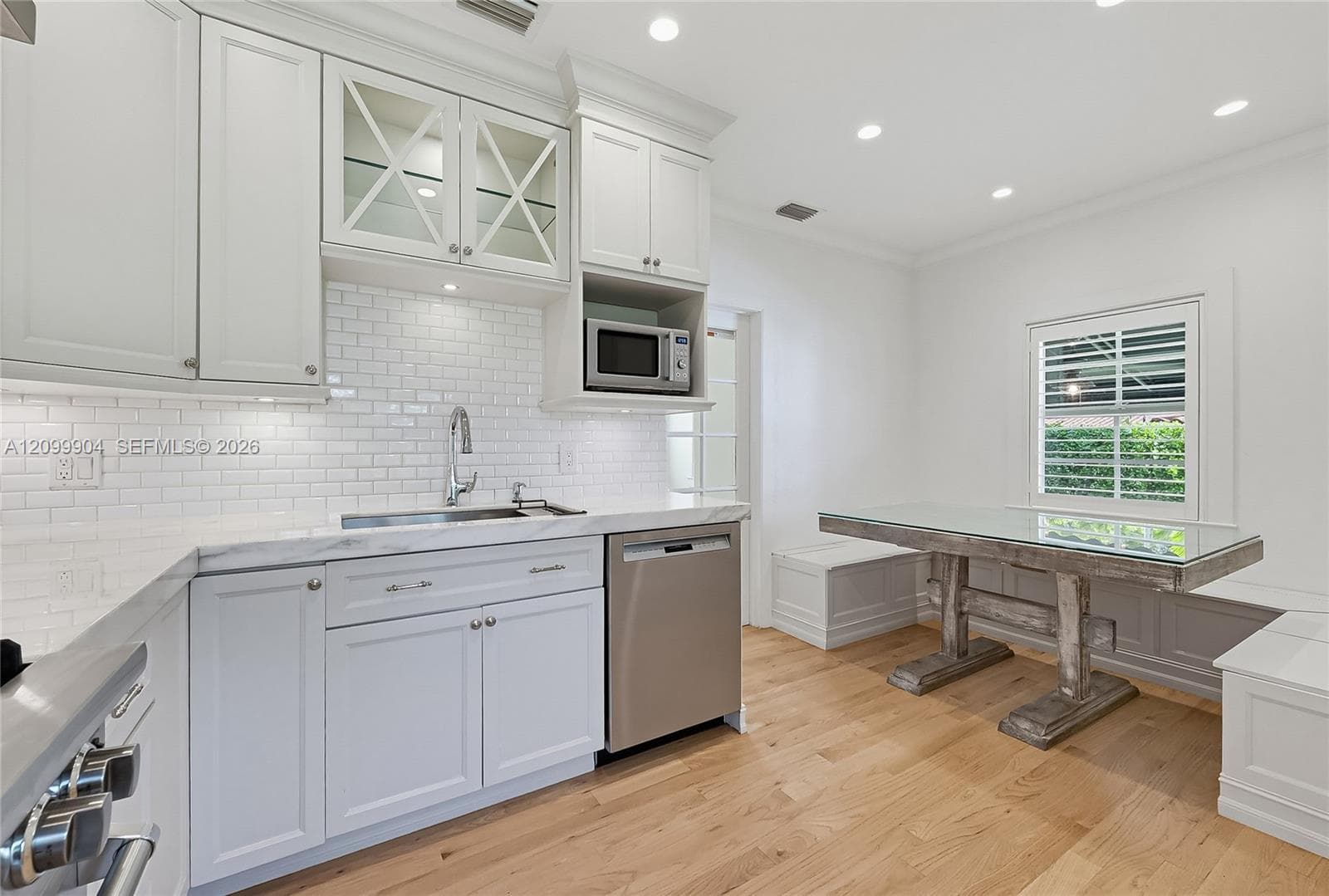 Kitchen featuring white shaker-style cabinetry, subway tile backsplash, stone-finish countertops, stainless steel appliances, and integrated bench seating