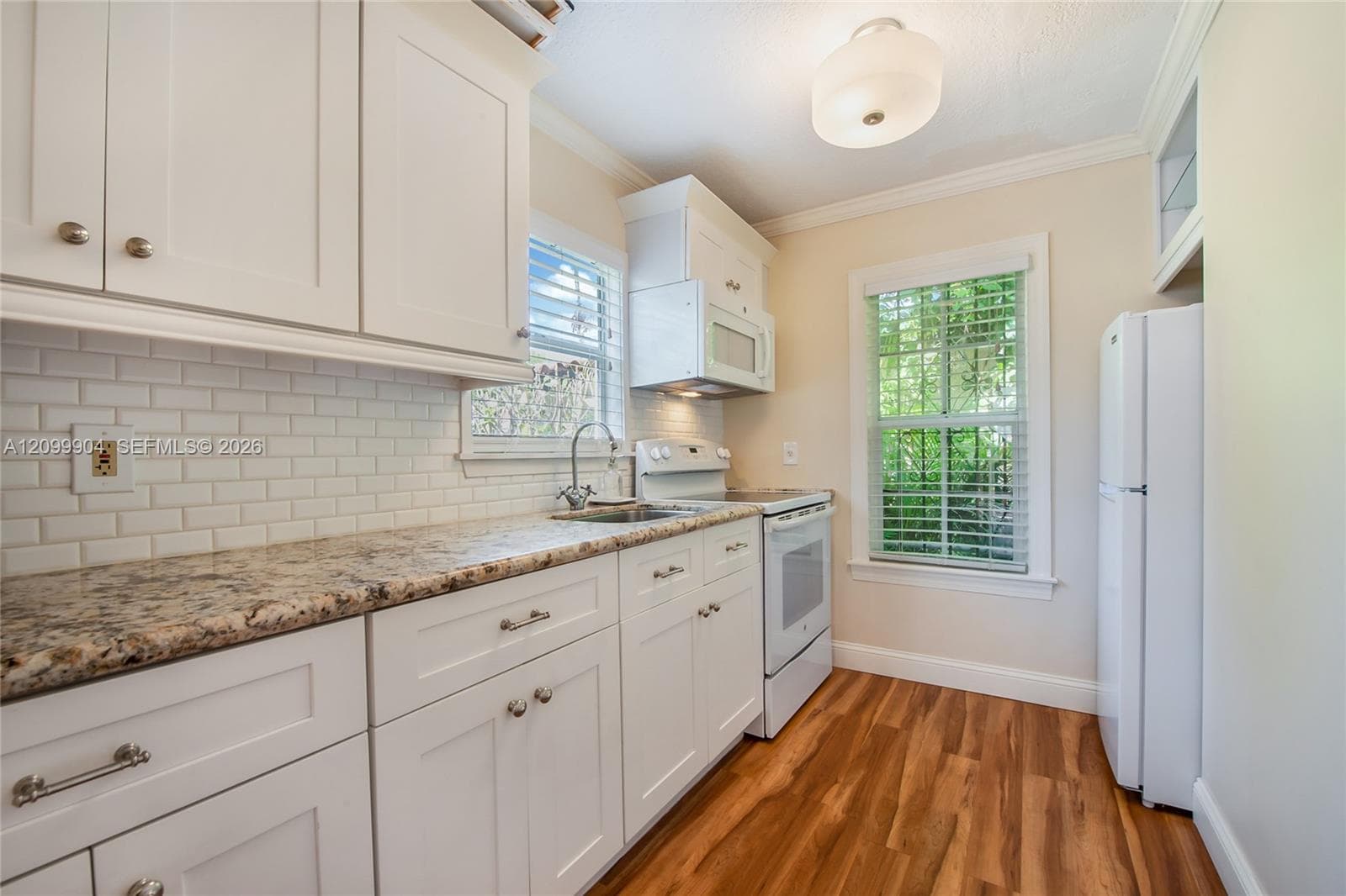 Kitchen featuring white shaker-style cabinetry, stone-patterned countertops, white subway tile backsplash, wood-finish flooring, and a flush-mount ceiling light