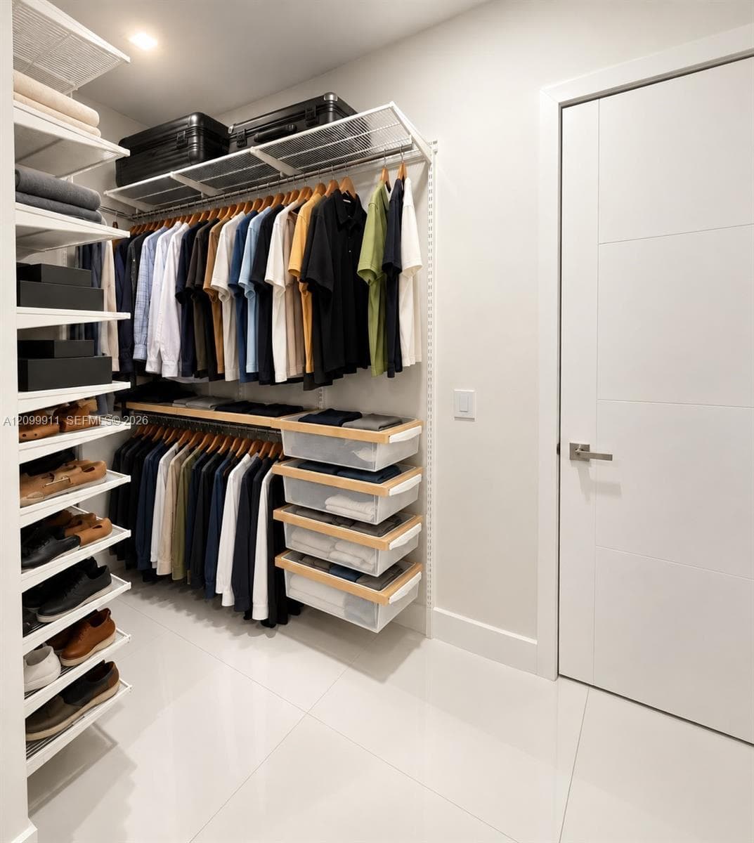 Custom closet organization system featuring white shelving, hanging rods, and integrated pull-out storage drawers, finished with large-format tile flooring and a modern paneled door