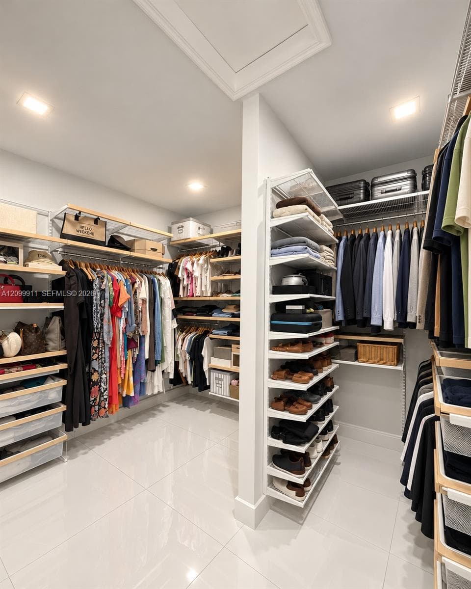 Walk-in closet featuring extensive built-in shelving, adjustable metal clothing rods, integrated drawer units, and light-reflecting tile flooring