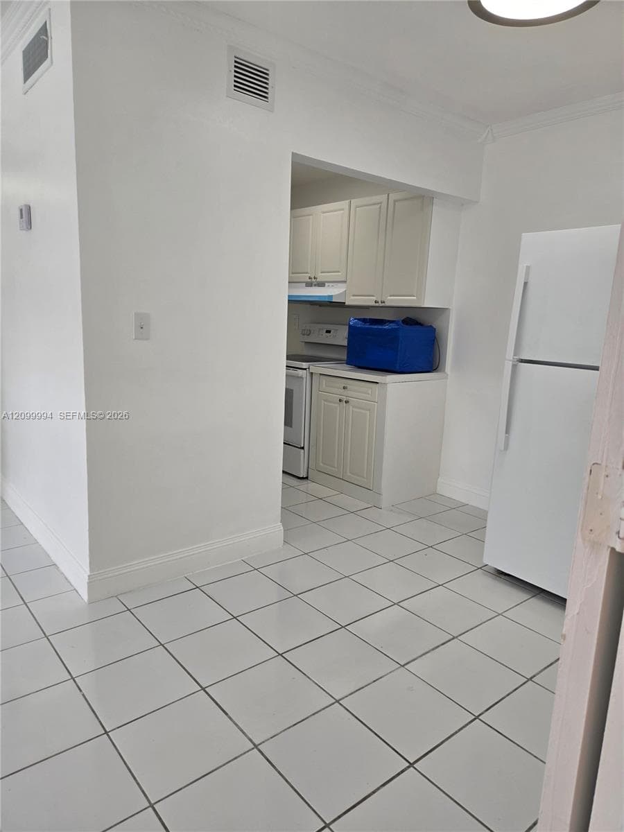 Recessed kitchen area with white cabinetry and appliances