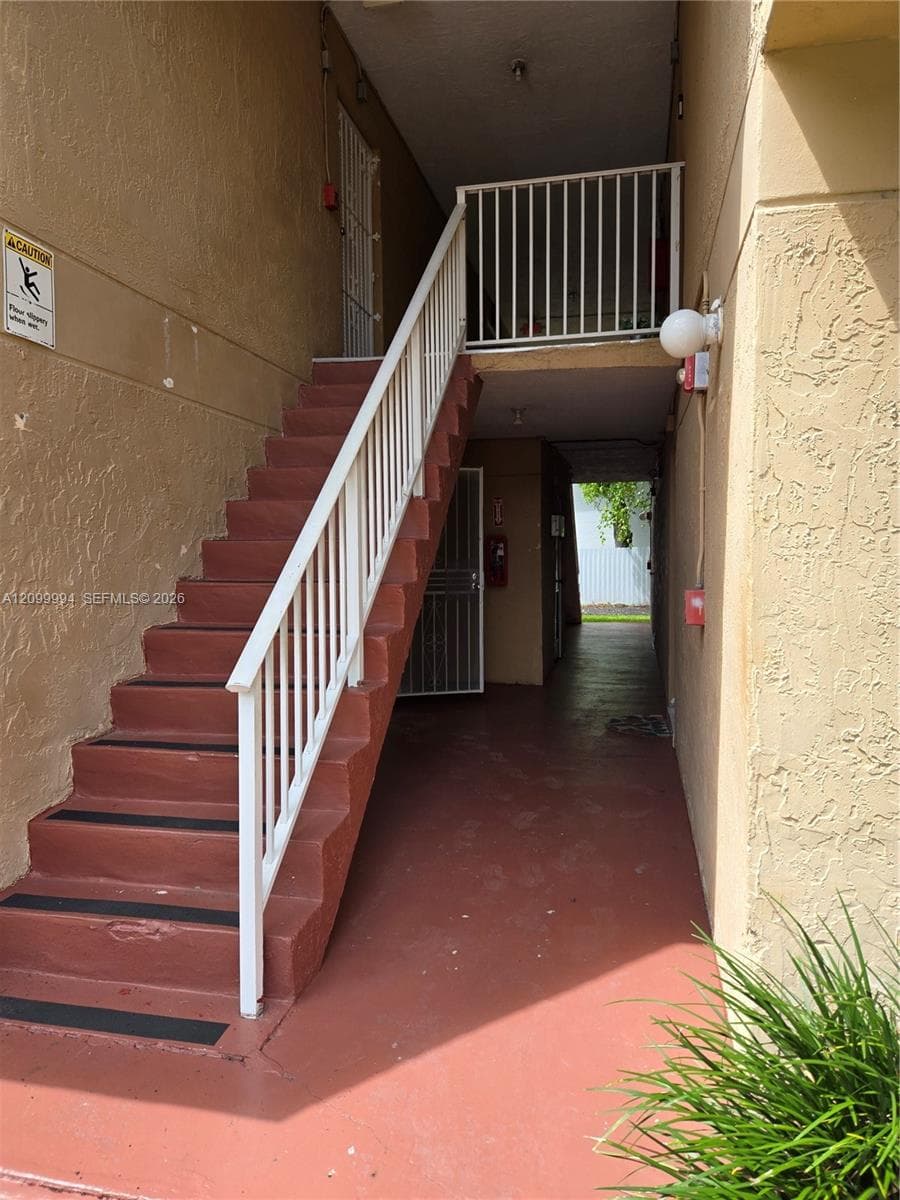 Exterior staircase with white metal railings, concrete steps featuring non-slip surfacing, and a covered ground-level landing