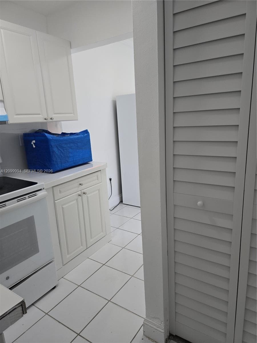 Kitchen featuring white cabinetry, solid-surface countertops, tile flooring, and a louvered closet door