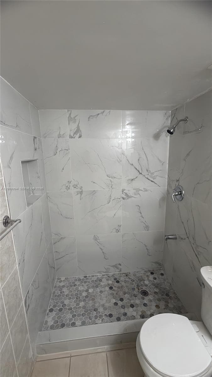 Walk-in shower with marble-look wall tiling, mosaic pebble flooring, and polished chrome fixtures