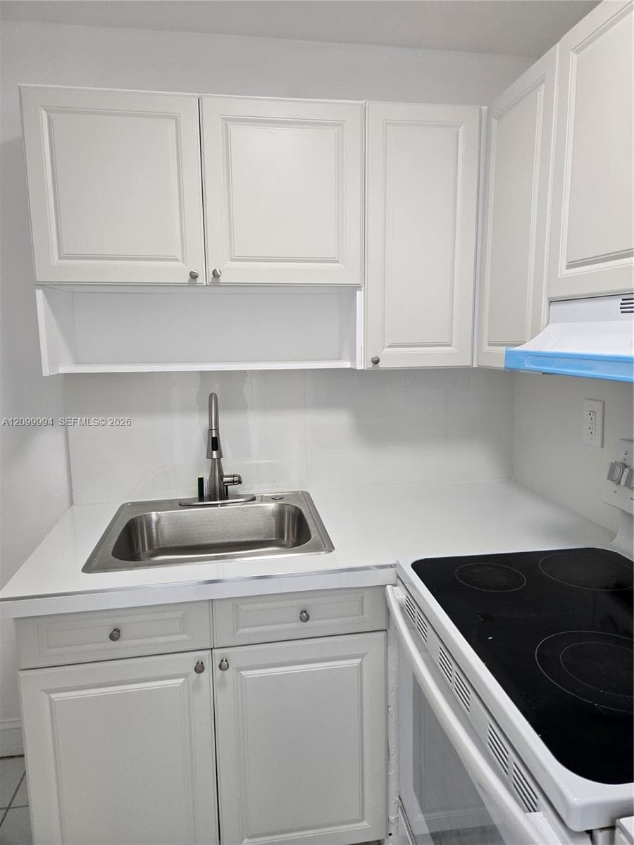 Kitchen featuring white cabinetry, solid surface countertop, stainless steel drop-in sink with a high-arch faucet, and an integrated electric cooktop