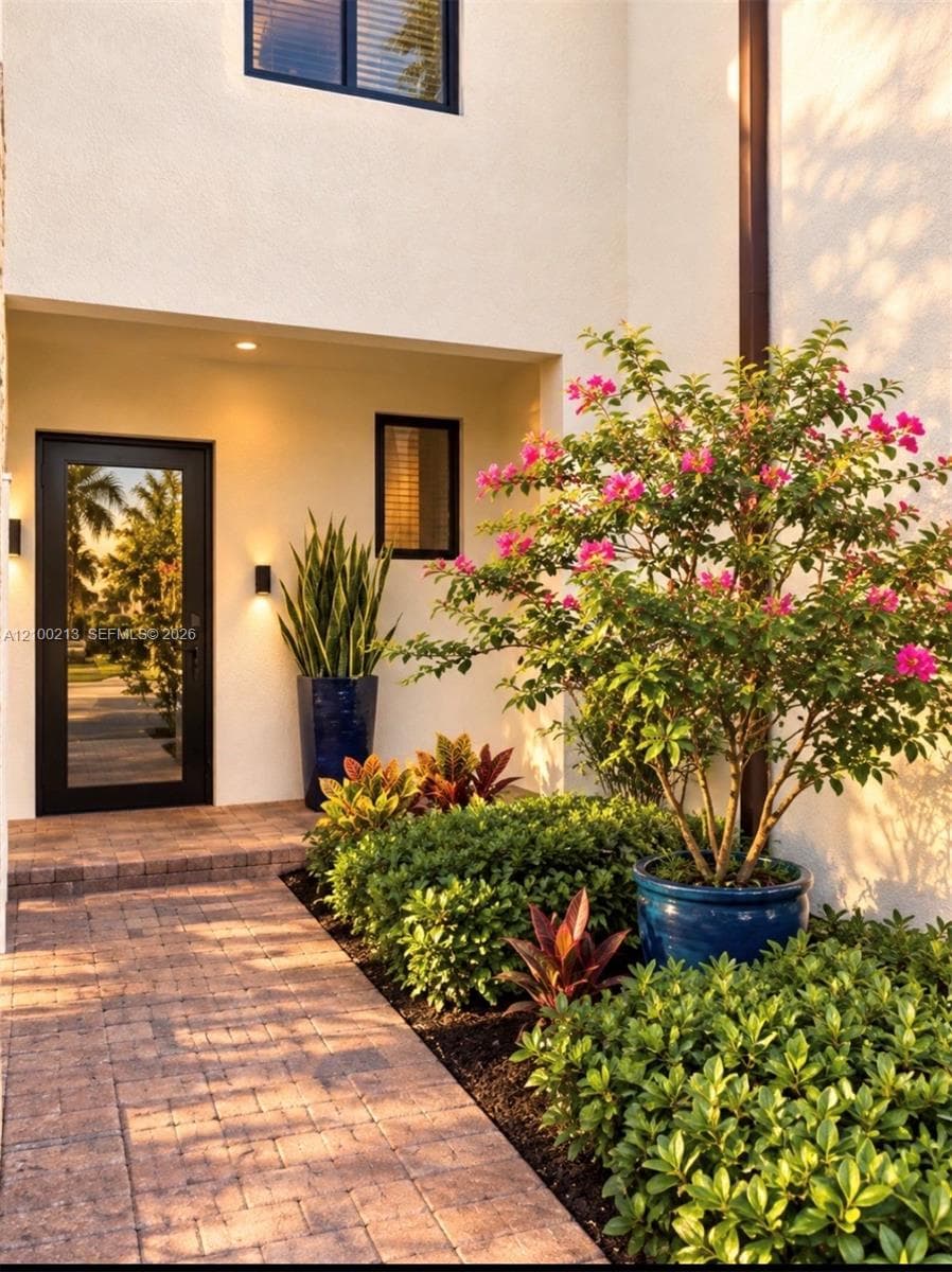 Covered entryway featuring smooth stucco exterior, full-lite glass front door with black frame, and paver walkway