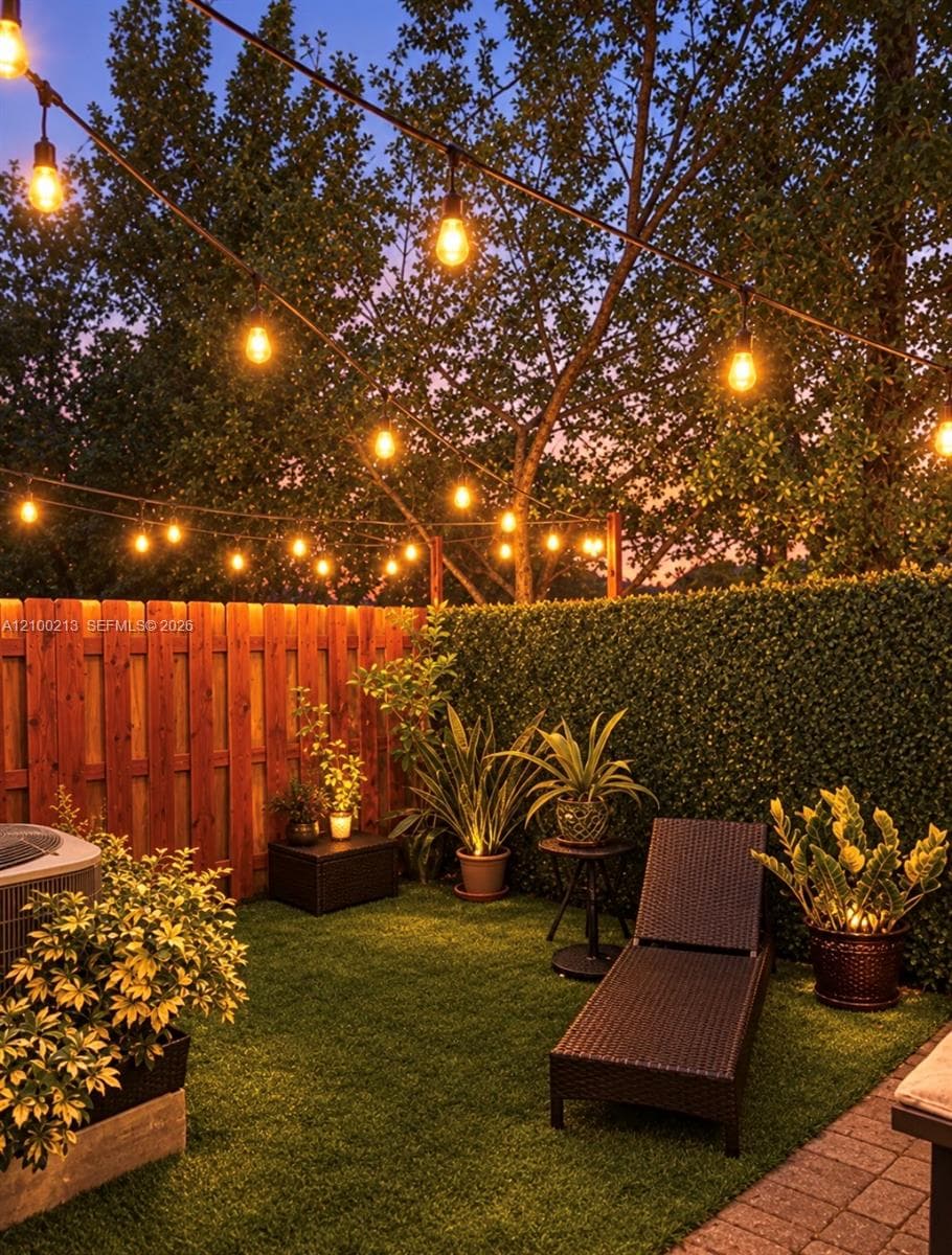 Private outdoor space featuring synthetic lawn, wood-panel fencing, integrated greenery screen, and overhead string lighting