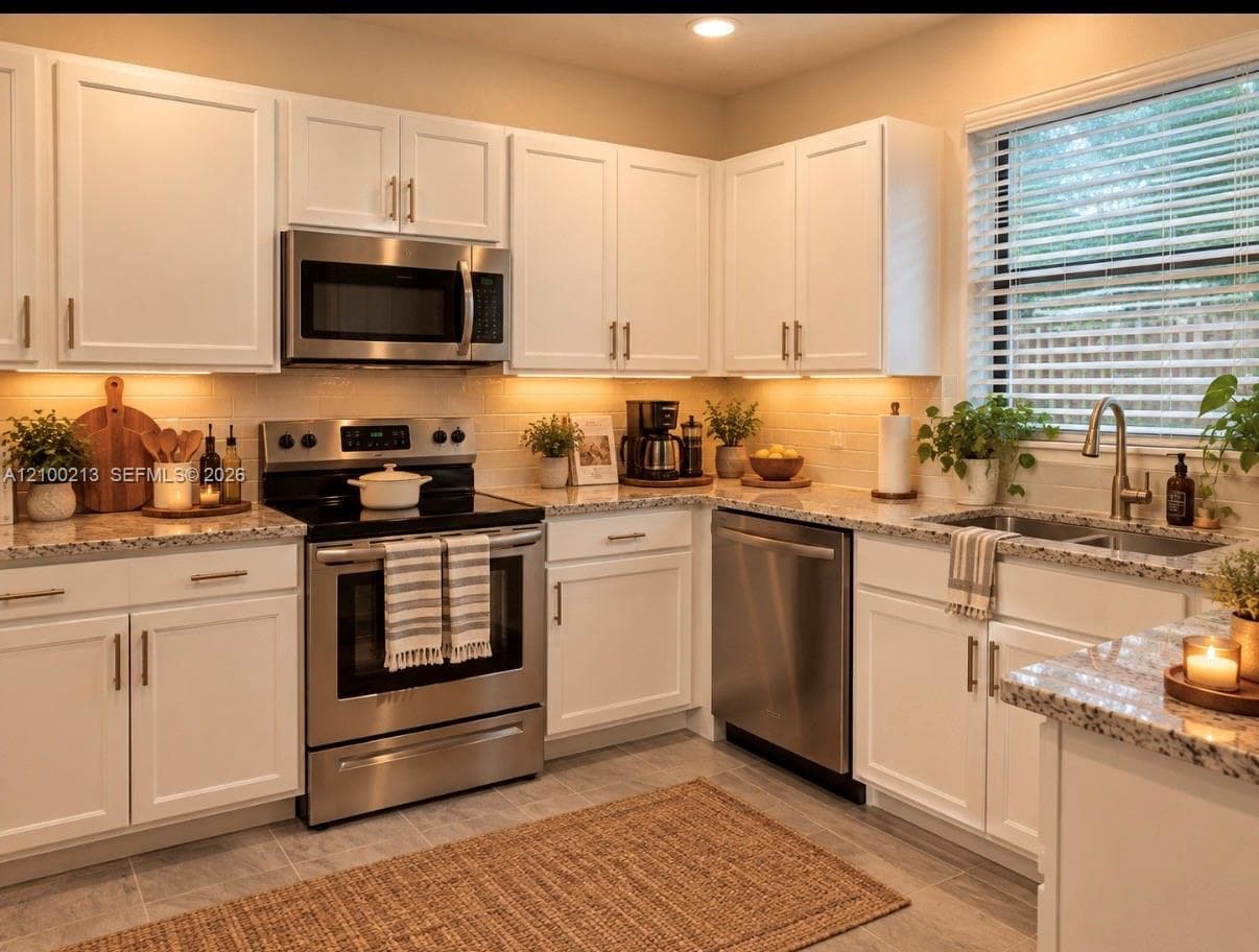Kitchen featuring white cabinetry, stone countertops, stainless steel appliances, and a double-basin undermount sink