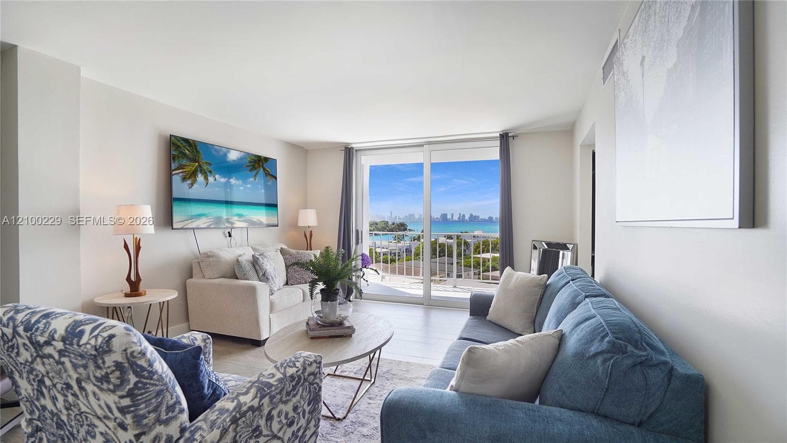 Living area featuring wood-finish flooring, neutral walls, and glass sliding doors opening to a balcony with coastal and city skyline scenery