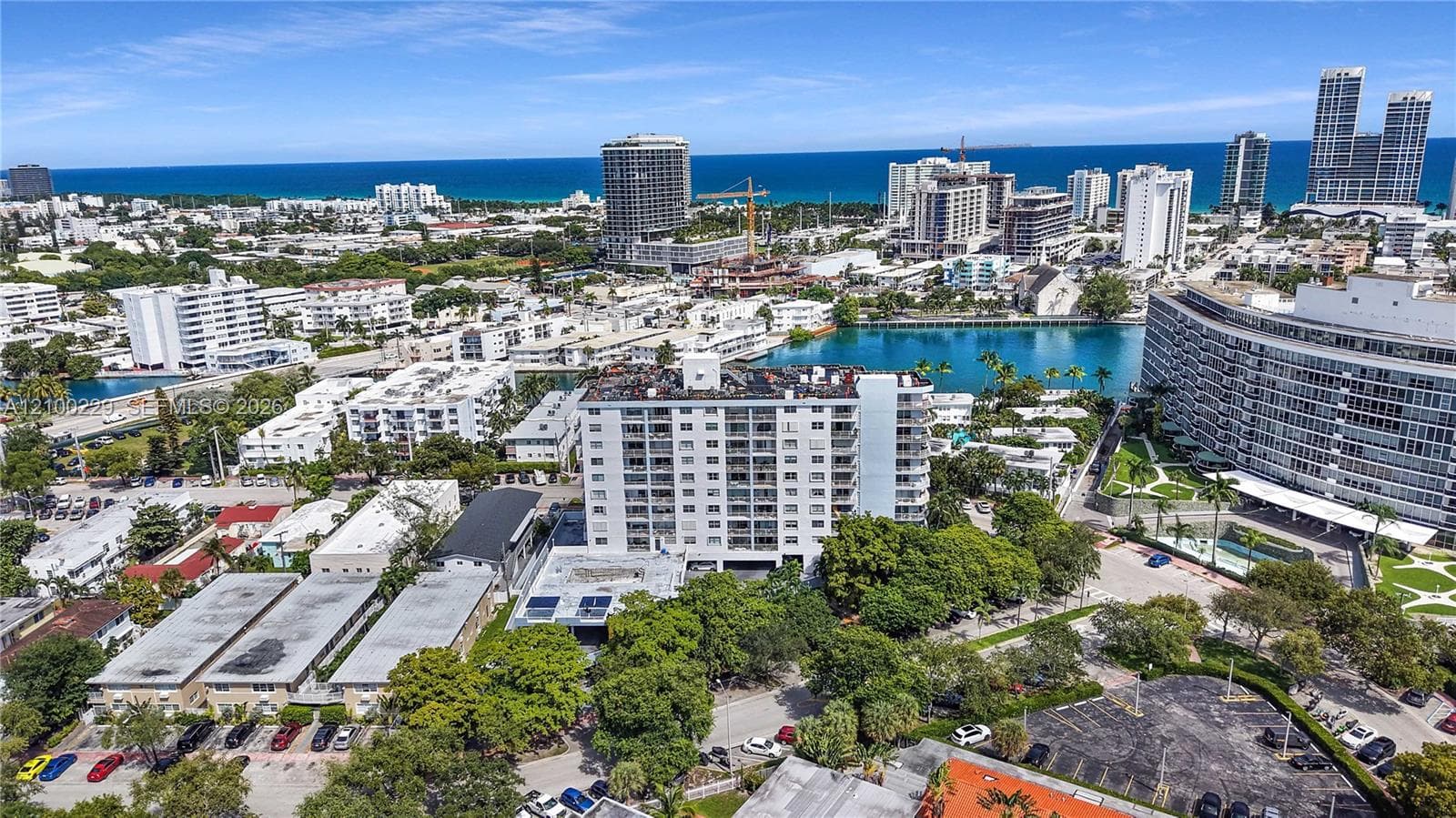 Aerial perspective of a high-rise condominium complex featuring a coastal location with shoreline proximity, mature tree cover, paved parking, and a mid-rise structural design