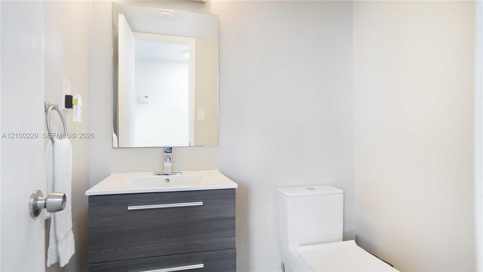 Modern vanity with dual drawers and a rectangular surface-mounted sink, wall-mounted rectangular mirror, chrome single-handle faucet, and dual-flush toilet