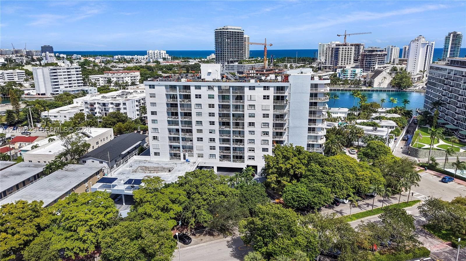 Mid-rise residential building featuring stacked private balconies, concrete construction, and exterior parking facilities situated within a coastal urban environment
