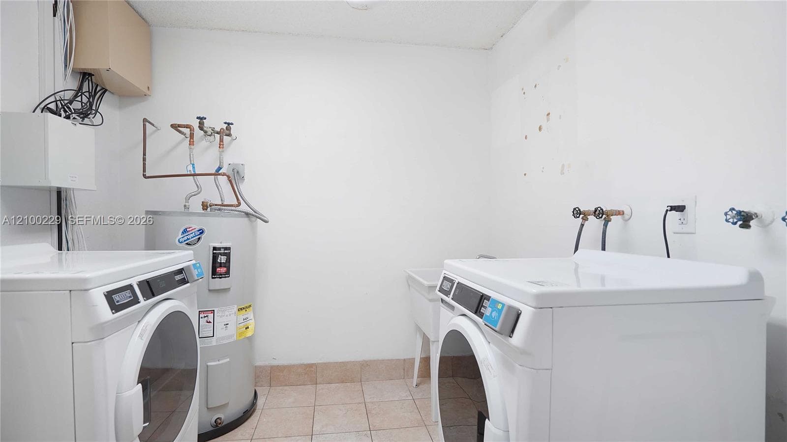 Utility space featuring ceramic tile flooring, a white basin sink, and an integrated water heater